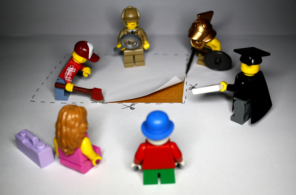 Lego figures, long haired woman in pink dress, scholar in hat and robe, sherlock holmes, investigate a square piece of cut paper.
